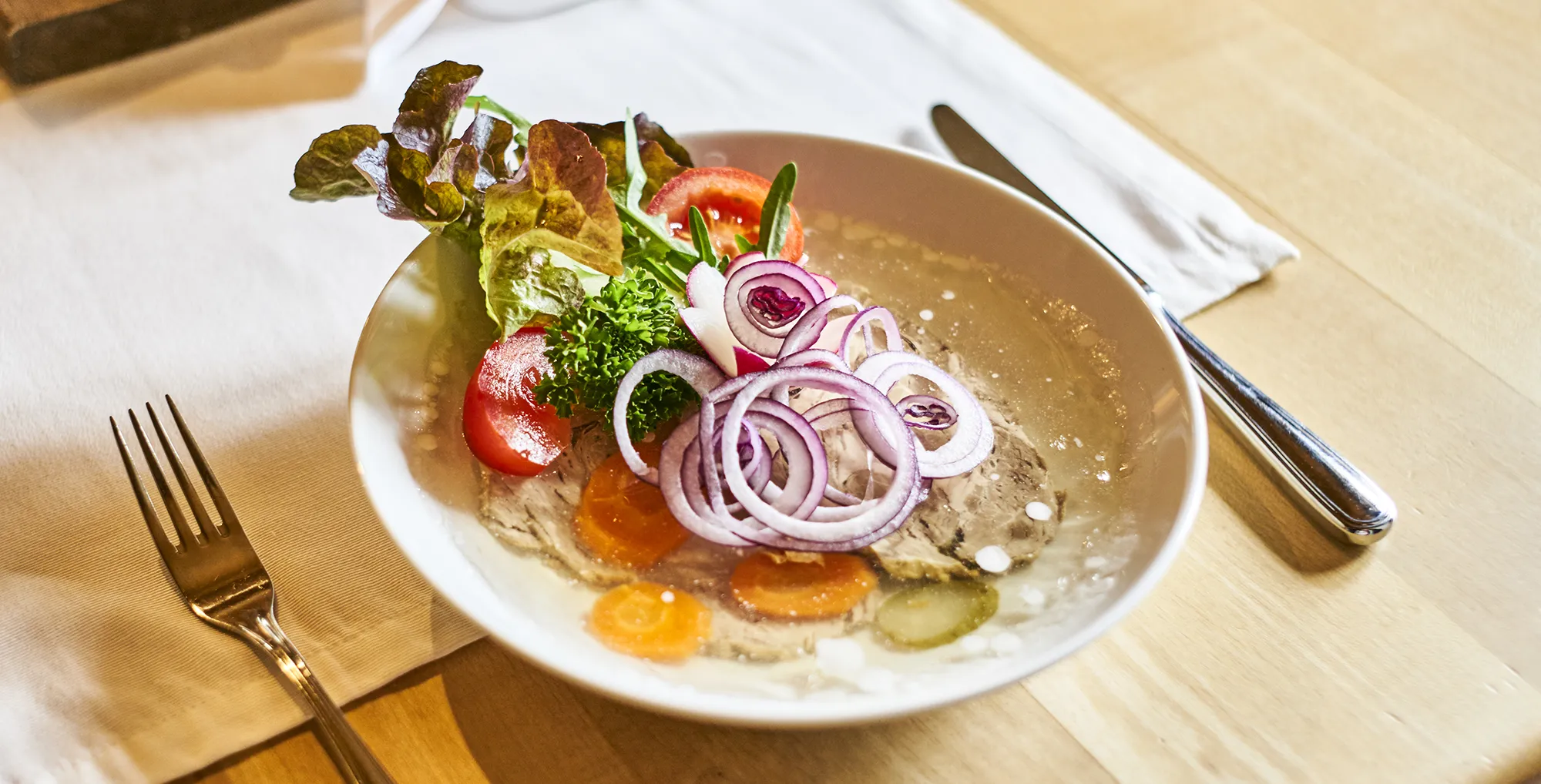 Ein Teller mit kaltem Braten, Gemüse und Gelee auf einem Tisch Tellersuelze