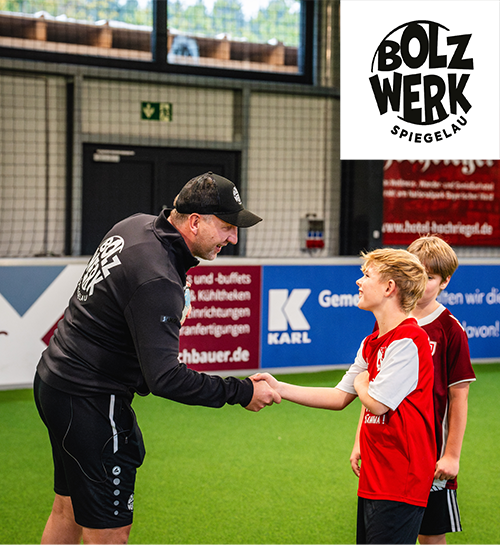 BOLZWERK Indoorfußballhalle Mann mit zwei Kindern in Indoor-Fußballhalle, der beim Kind "abklatscht"