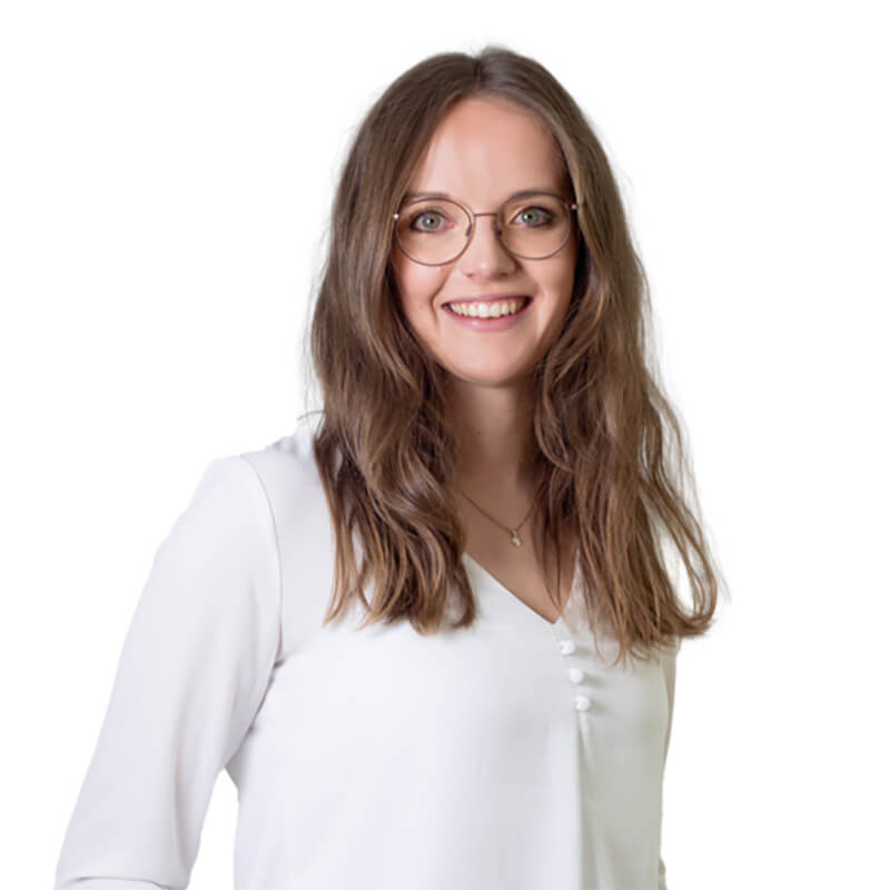 Andrea Kralik, Verwaltung Spiegelau Das Bild zeigt die lächelnde Mitarbeiterin, Andrea Kralik, mit langen, lockigen Haaren, in weißer Bluse.