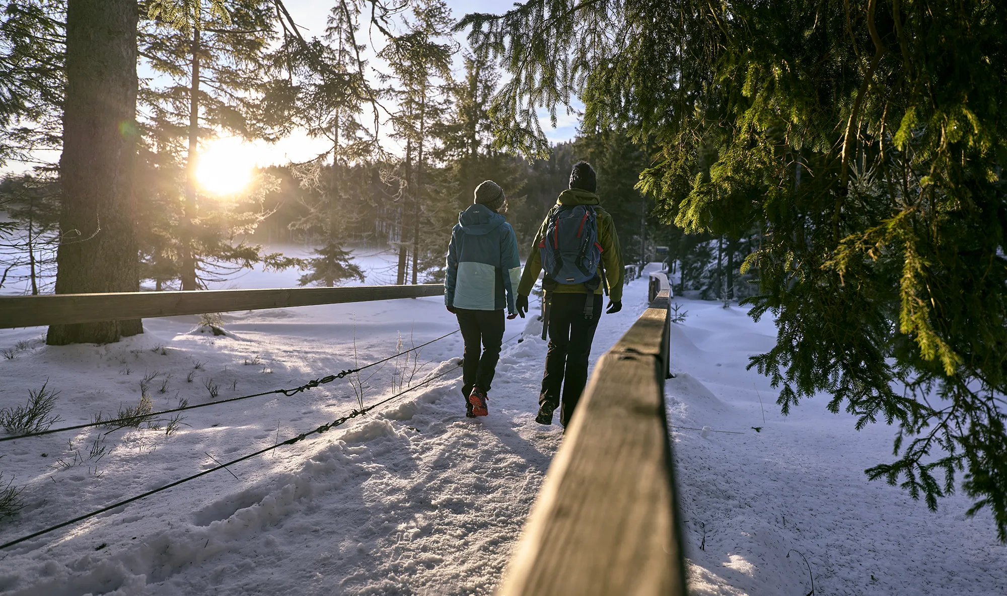 Zwei Urlauberinnen unternehmen eine Winterwanderung rund um den Großen Arbersse bei Sonnenuntergang. Zwei Frauen wandern auf verschneitem Steig um den Arbersee