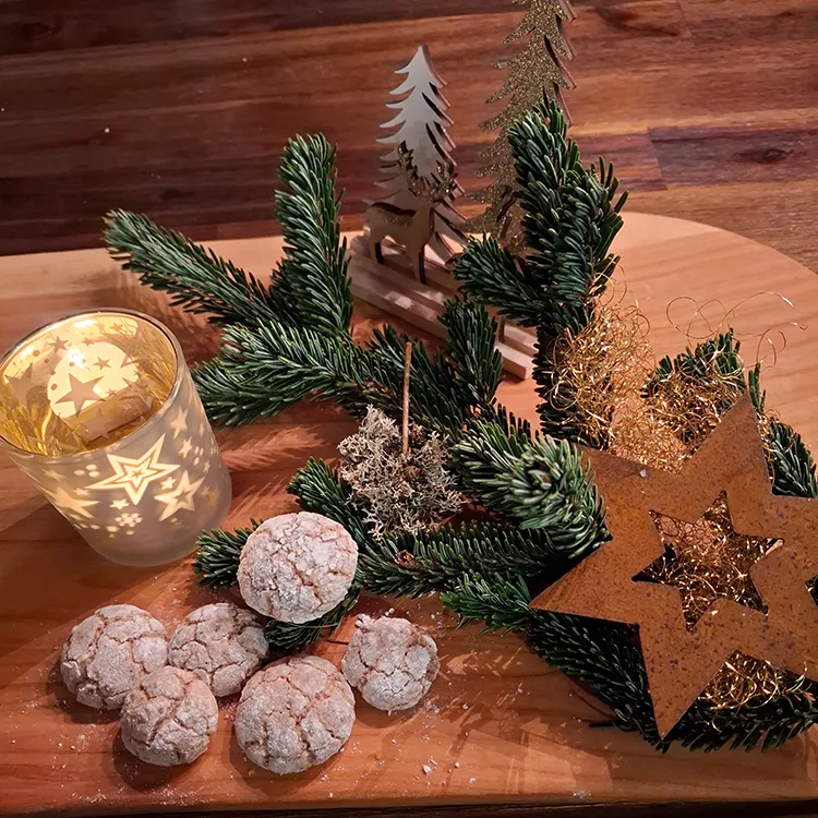 Festliche Weihnachtsdekoration mit köstlichen Plätzchen Ein rustikales Holzbrett mit festlichen kleinen Schokoladenbroten, Tannenzweigen und einer leuchtenden Kerze in einem Glas mit Sternen.