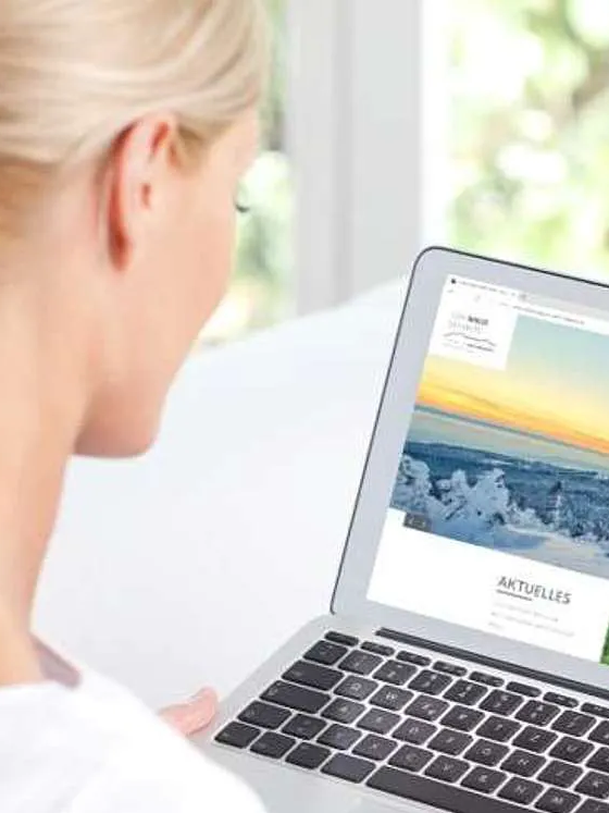 Frau plant ihren Urlaub am Laptop in einem hellen Raum Frau sitzt vor Laptop