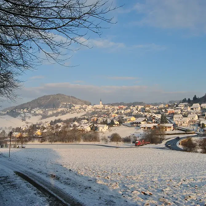 Winterwunderland rund um den Markt Schönberg Im Vordergrund ein Wanderpfad, der über den winterlichen Weg führt, während Schönberg im Hintergrund in der Sonne erscheint.